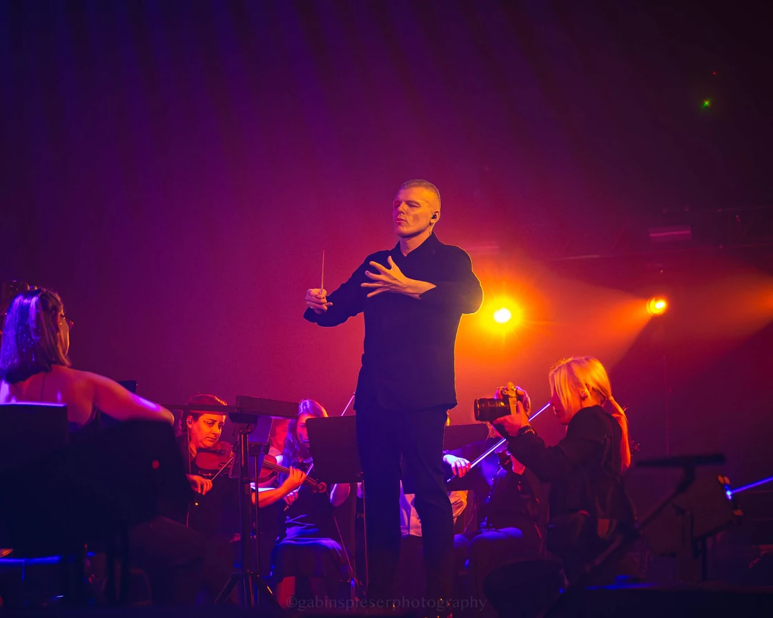 Electro Symphony — Un chef d’orchestre dirige les musiciens dans une lumière orange et violette.