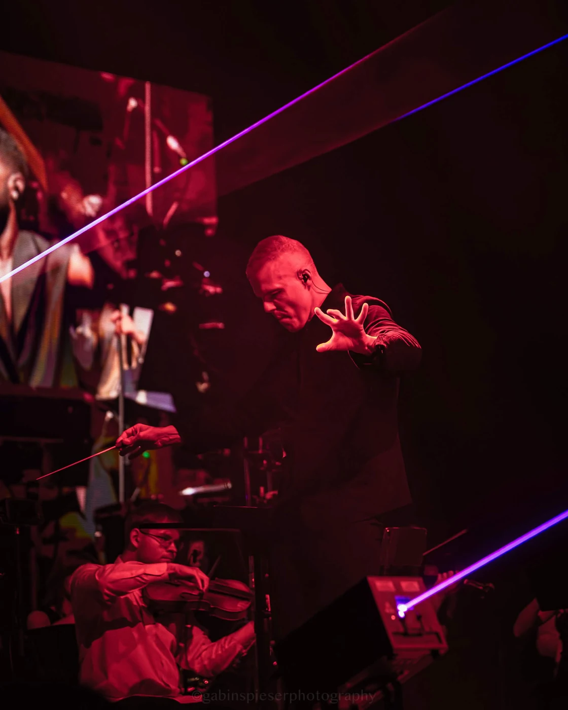 Electro Symphony — Un chef d’orchestre tend la main au milieu de lumières rouges et de lasers.