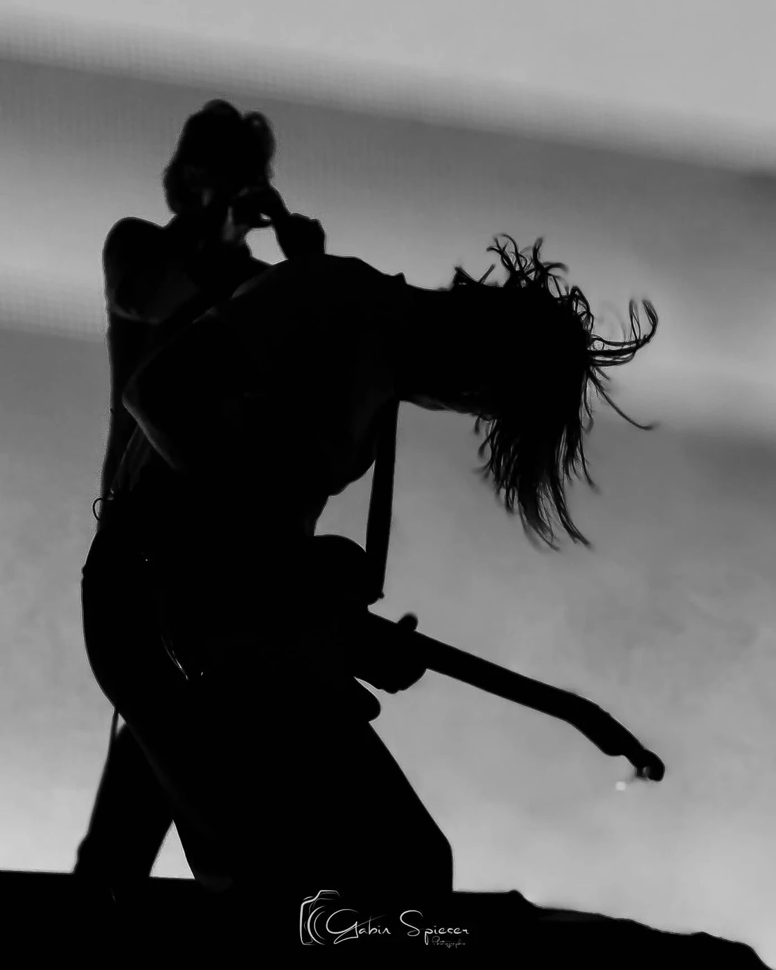 Feu! Chatterton — En noir et blanc, la silhouette d’un guitariste se plie en avant, les cheveux projetés dans la lumière.