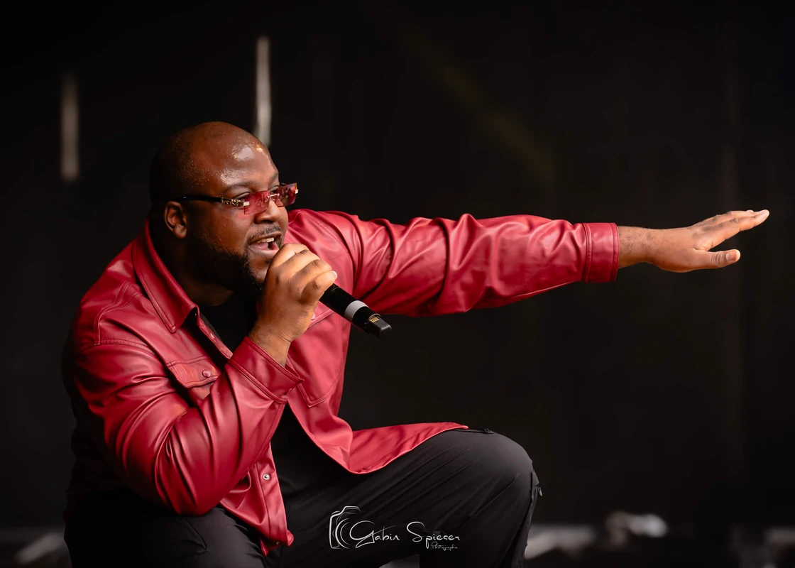 LOKYTO — Un chanteur en veste rouge tend le bras vers le public, accroupi au bord de la scène.