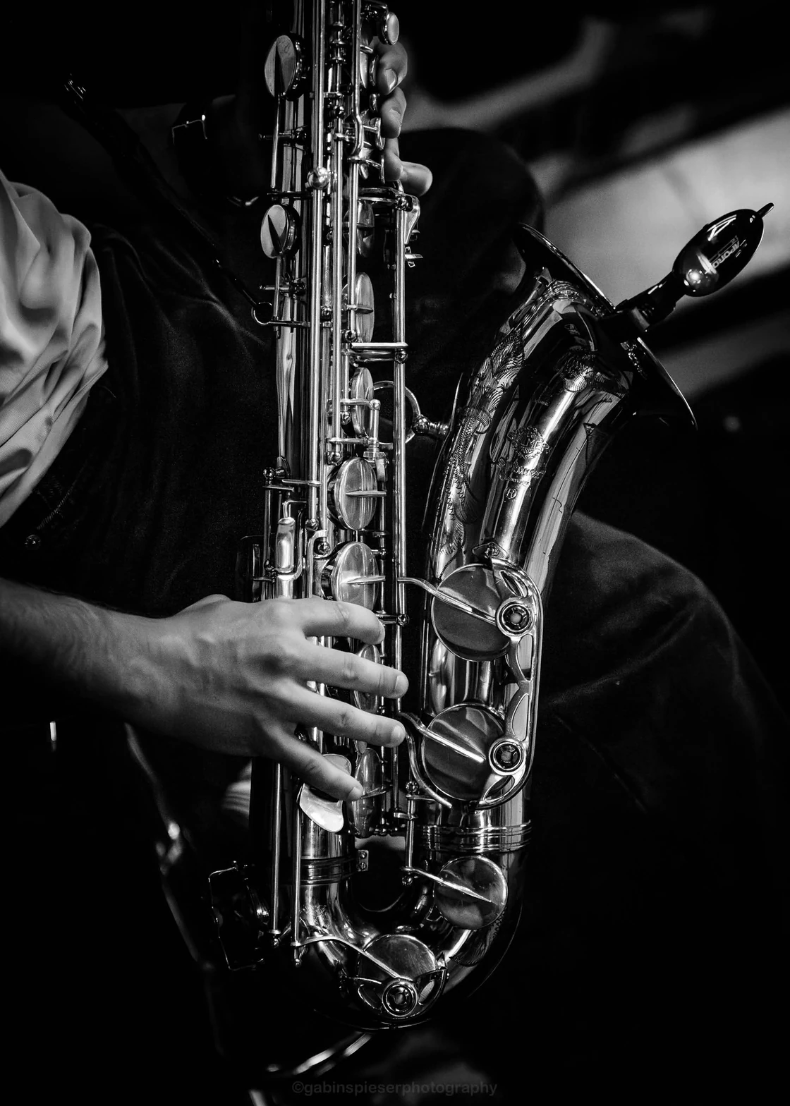 Noa Sax — En noir et blanc, gros plan sur les mains d’un musicien et les reflets de son saxophone. V and B Saint-Memmie · juillet–août 2026.